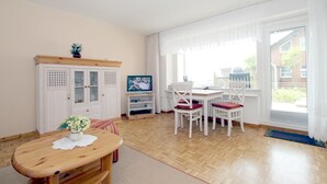 Huoneessa on puinen pöytä, valkoiset tuolit, kaappi ja televisio.