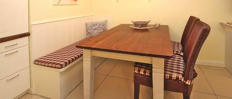 Un comedor con mesa de madera, bancos y sillas de mimbre.