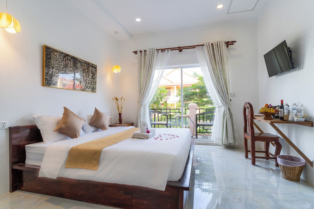 Une chambre d’hôtel avec un grand lit, un téléviseur fixé au mur et un balcon donnant sur un paysage verdoyant.