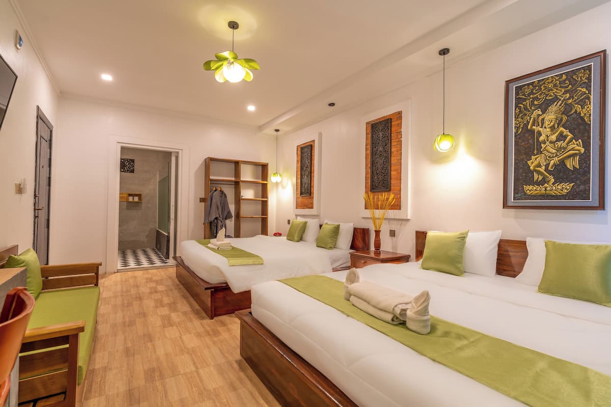 Une chambre d’hôtel avec deux lits, un banc en bois, un bureau et une salle de bain avec douche.