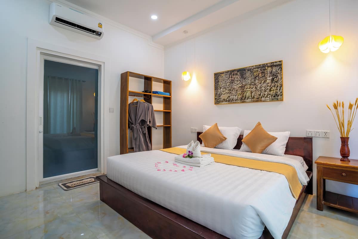 Une chambre d’hôtel comprenant un lit, une armoire, une table de chevet, un climatiseur fixé au mur et un tableau.