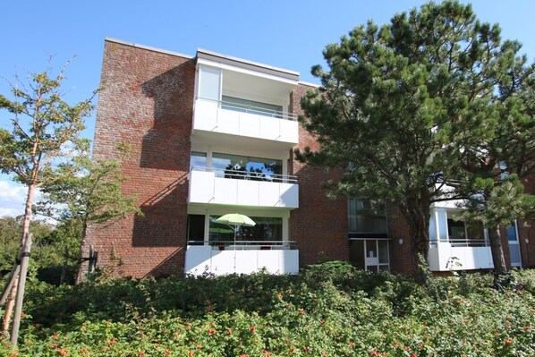 A two-story building with a brick facade, a balcony on the upper floor, and a green umbrella on the ground floor. - Ferienwohnung mit 2- Zimmern und Balkon (Wyk auf Föhr)