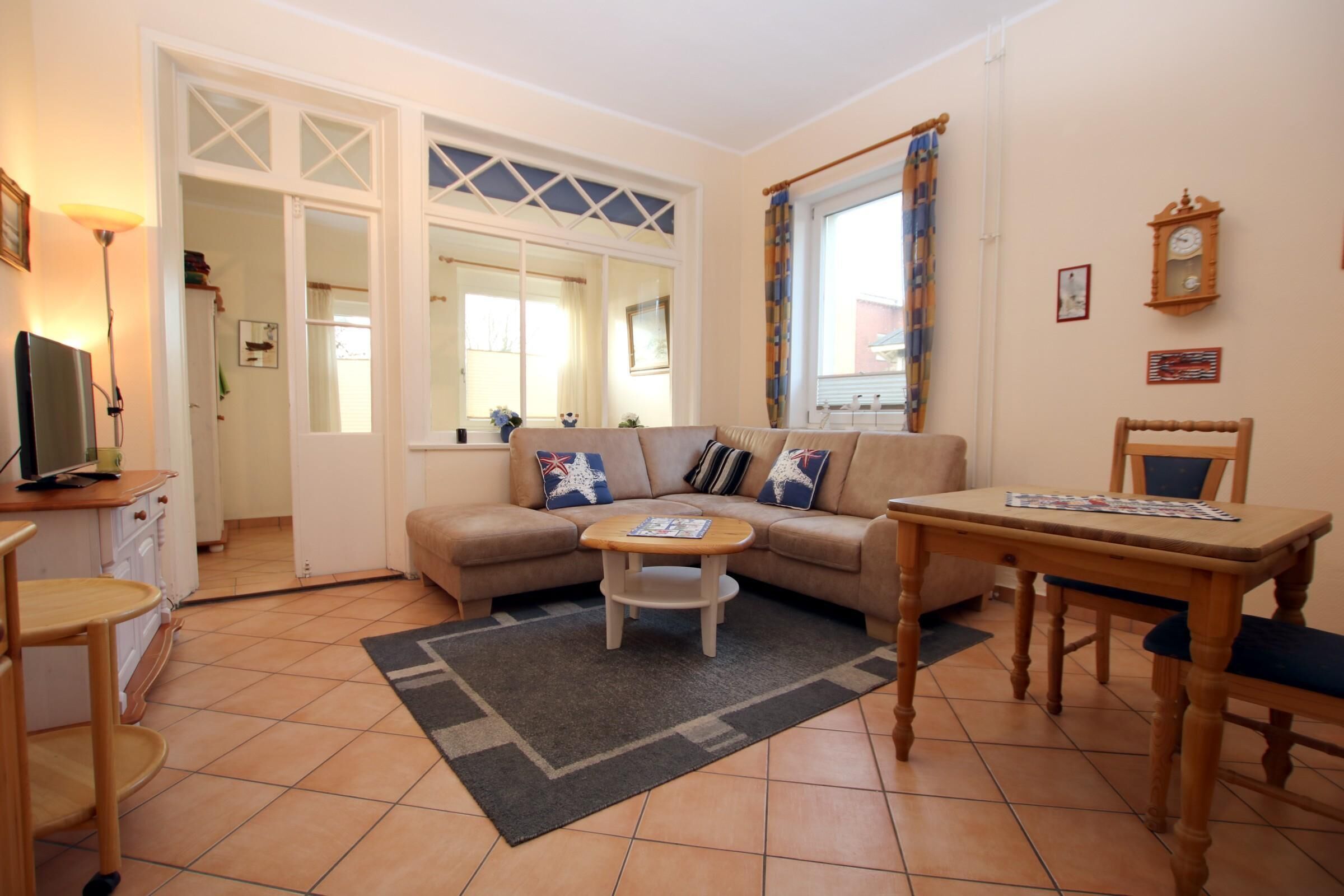 Un salon confortable avec un canapé, une table basse et une table à manger. On y trouve un téléviseur posé sur un meuble, une lampe et une fenêtre avec des rideaux.