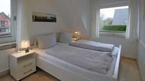 Et soveværelse med to senge, et natbord med en lampe og et billede på væggen.