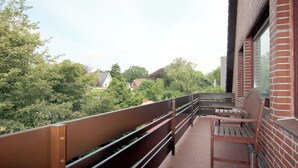 En balkon med træbænk og bord, der kigger ud over et boligområde med træer og huse.