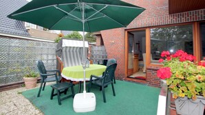 Un patio con una mesa y sillas, una sombrilla verde y un edificio de ladrillo al fondo.