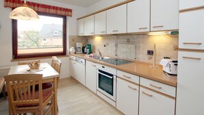 Una cocina con armarios blancos, encimera de madera, una mesa de comedor con sillas y una ventana con persianas.