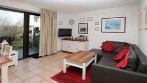 A modern living room with a sofa, a coffee table, a TV, and a kitchen area with cabinets and a countertop.