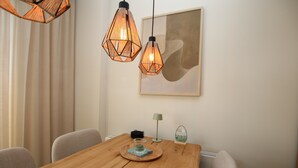 A dining area with a wooden table, two hexagonal pendant lights, a framed abstract painting, a small lamp, and a glass display on the wall.
