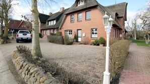 A traditional brick house with a thatched roof, a gravel driveway, and a stone wall.