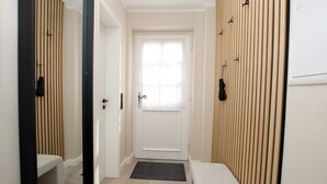 A narrow hallway with a white door at the end, wooden paneling on the walls, a bench, and a small step leading to the door.