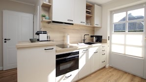 A modern kitchen with white cabinetry, a built-in oven, a sink, and a window with a view of the outside.