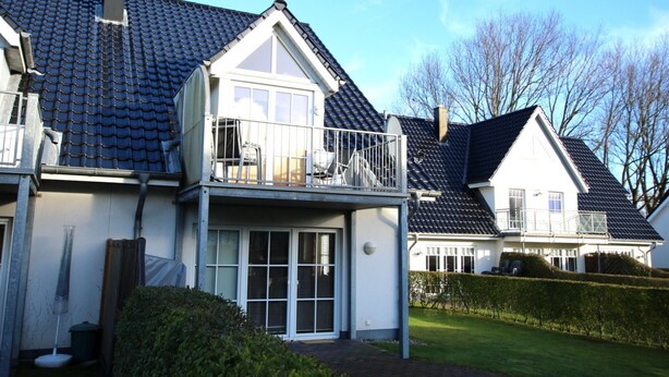 Ein zweistöckiges Haus mit Balkon, überdachter Terrasse und gepflegtem Garten.