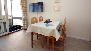 Un comedor con una mesa lista para dos personas, un televisor montado en la pared y un ventanal corredero que da a un espacio exterior.