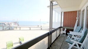 Un balcón con vistas a la playa, sillas reclinables blancas y un sofá verde.