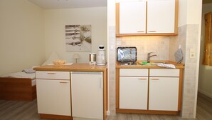 Una cocina compacta con refrigerador, microondas y pileta. Hay una pequeña mesa de comedor y una cama en la habitación contigua.