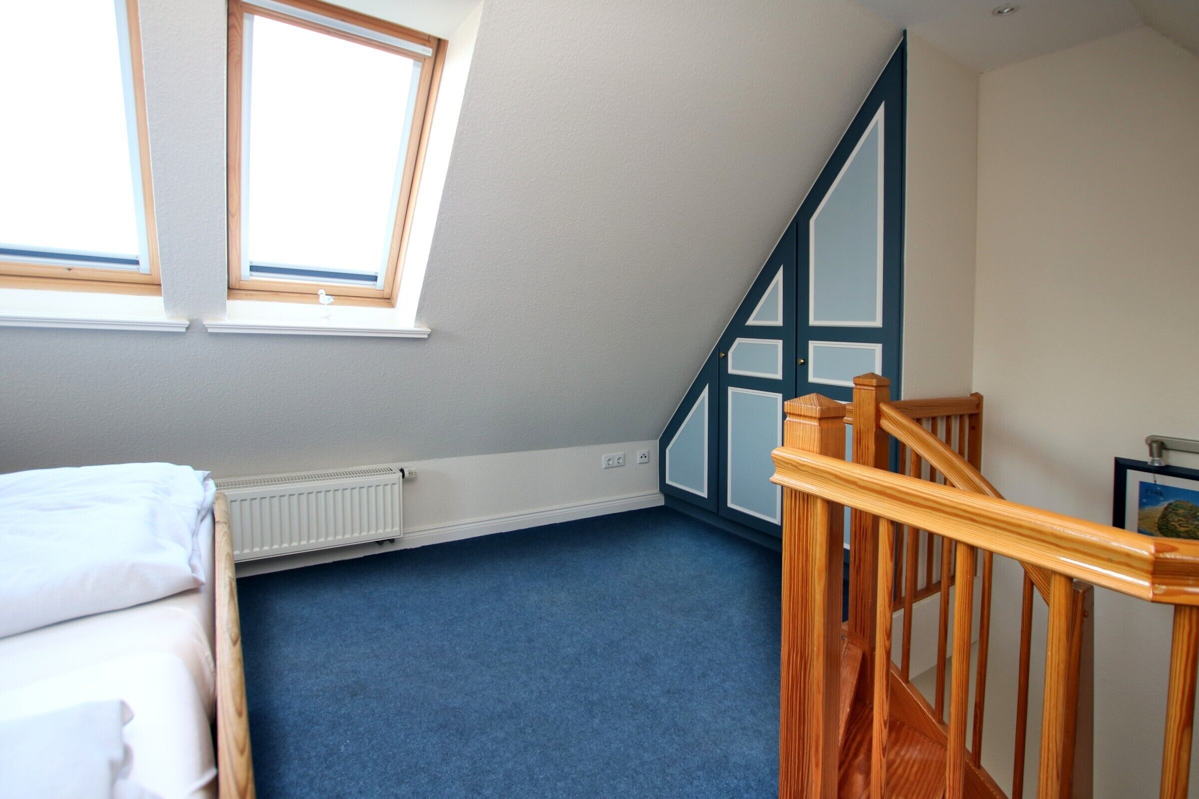 A bedroom with a sloped ceiling, a wooden staircase, and a radiator.