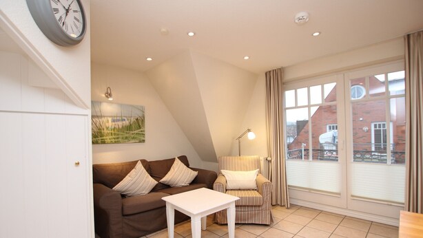 Ein Wohnzimmer mit einem braunen Sofa, einem weißen Tisch, einem gestreiften Sessel und einem großen Fenster mit Vorhängen.