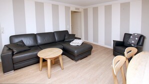 Una sala moderna con un sofá de cuero negro, una mesa de centro redonda de madera y un sillón negro con un plaid estampado de estrellas.
