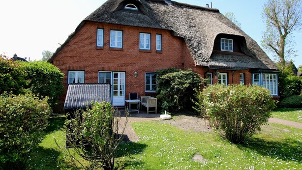 A traditional brick house with a thatched roof, a small garden, and a visible outdoor seating area. - Ferienwohnung mit 3- Zimmern auf ca. 49m² (Wyk auf Föhr)