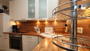 A modern kitchen with white cabinets, a stainless steel oven, a wooden countertop, and a unique circular light fixture. - Ferienwohnung mit 3- Zimmern auf ca. 50m² (Wyk auf Föhr)
