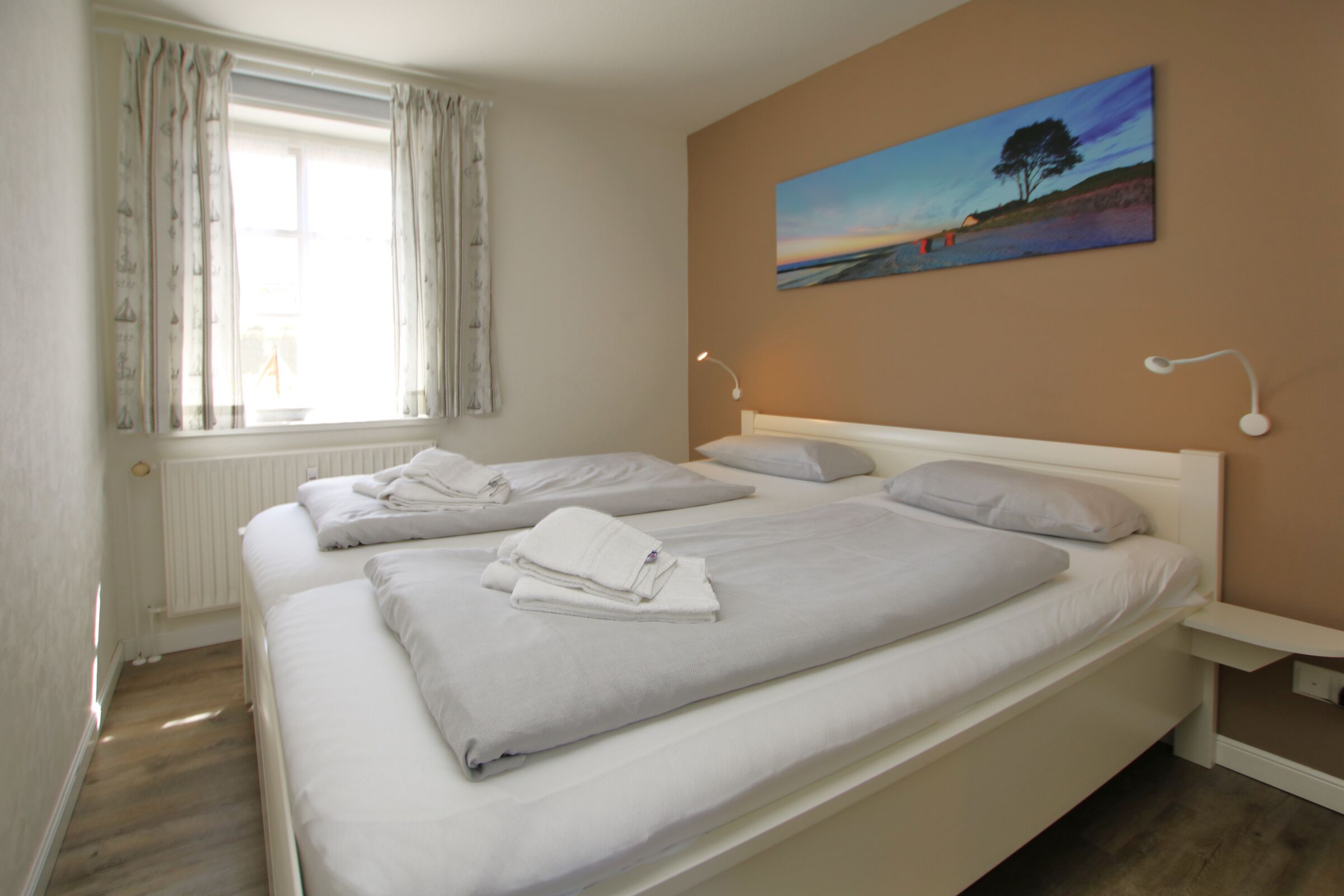 A hotel room with two beds, a window with curtains, a painting on the wall, and a bedside table with a lamp.