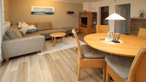 A modern living room with a sofa, round dining table, and wicker chairs. - Ferienwohnung mit 3- Zimmern auf ca. 50m² (Wyk auf Föhr)