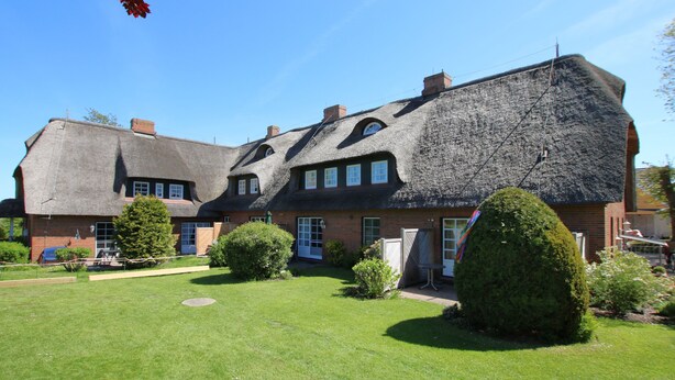 A large, thatched-roof house with a well-maintained lawn and several windows. - Ferienwohnung mit 3- Zimmern auf ca. 50m² (Wyk auf Föhr)