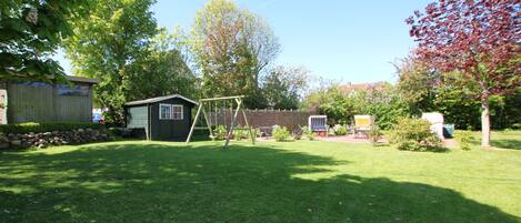 A backyard with a swing set, a shed, and a tree.