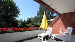 Ein überdachter Patio-Bereich mit weißen Liegestühlen, einem gelben Sonnenschirm und einer Ziegelwand.