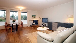 Ein modernes Wohnzimmer mit Holztisch, einer Couch, einem Fernseher und einer Küchenzeile.