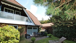 A two-story house with a patio area, a lawn, and a wooden lounge chair. - Ferienwohnung mit 3 Zimmern, Sehr Komfortabel und Komplett Renoviert auf 58 m² (Wyk auf Föhr)