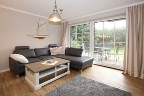 Un salon moderne avec un canapé d’angle gris, une table basse en bois et une décoration sur le thème de la voile.