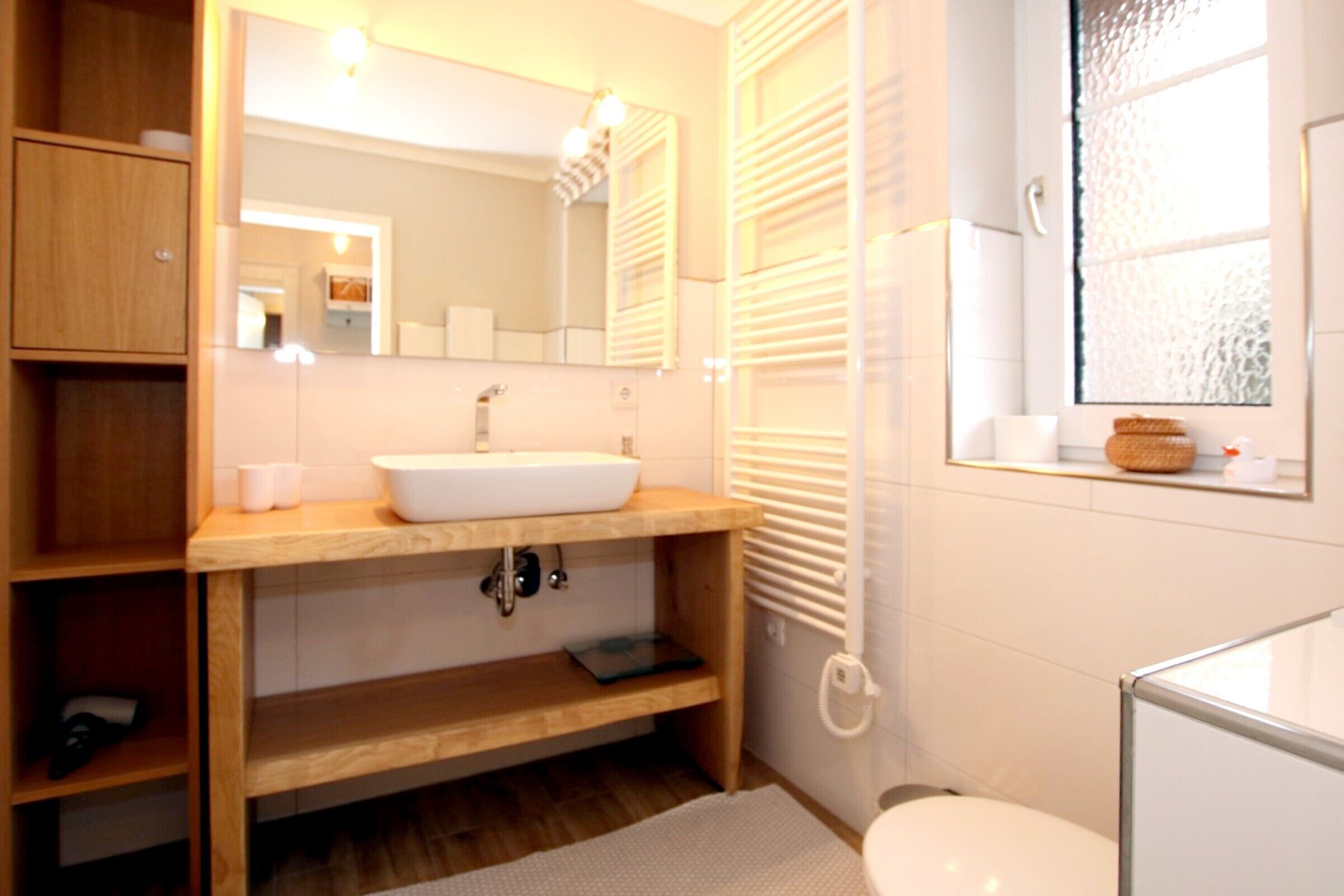 Un baño moderno con un mueble de tocador de madera, un lavabo blanco y un espejo grande.