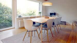 A modern dining area with a wooden table and chairs, large windows, and a view of greenery outside. - Ferienwohnung mit Garten, Insgesamt 6- Zimmern, 4 SZ und 3 Bädern auf ca. 160qm (Wrixum)