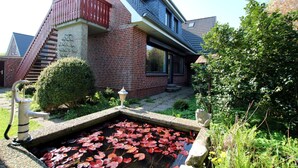 A house with a red brick exterior, a balcony, and a small pond with lily pads. - Ferienwohnung mit Garten, Insgesamt 6- Zimmern, 4 SZ und 3 Bädern auf ca. 160qm (Wrixum)