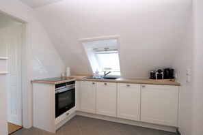 A compact kitchen with white cabinets, a built-in oven, a window above the sink, and a countertop with a kettle and coffee maker.