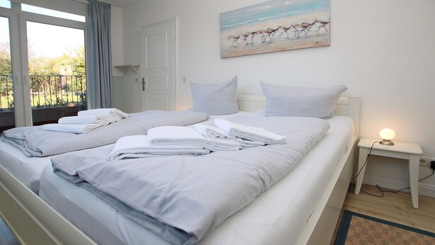 Een net opgemaakt bed met opgevouwen handdoeken, een nachtkastje met een lamp, en een schilderij van paarden aan de muur.