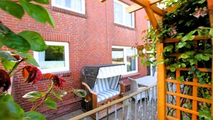 Een bakstenen gebouw met een terras, voorzien van een houten stoel, een tafeltje en een metalen hek.