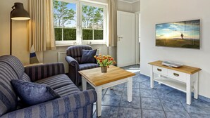 Una sala de estar con un sofá, un sillón, una mesa de centro y un televisor en la pared.