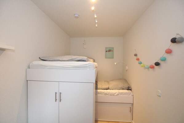 A small, well-lit room with a bunk bed, a wardrobe, and a wall-mounted light fixture. - Ferienwhg. in Wyk mit 3- Zimmern, ca. 58 m² im EG mit Südterrasse und Garten (Wyk auf Föhr)