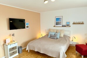 A bedroom with a bed, bedside tables, a TV, and wall decorations. - Ferienwohnung mit 1- Zimmer auf ca. 43m² in 1. Strandlage mit Meerblick (Wyk auf Föhr)