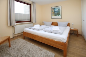 Una camera da letto con un letto in legno, biancheria bianca, un tappeto soffice, un comodino con una lampada e una finestra con tende.