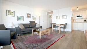 A modern living room with a sofa, coffee table, and dining area. There is a kitchen visible in the background. - Ferienwhg. Wyk, mit 2 Zimmern, ca. 52 m² im 1.og mit Meerblick auf die Halligen (Wyk auf Föhr)