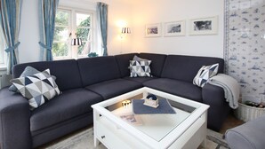 A modern living room with a dark grey sofa, a white coffee table, and a window with blue curtains. - Reihenhausscheibe mit 3- Zimmern (Wrixum)