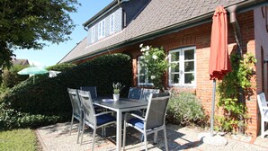 An outdoor patio with a table and chairs, a potted plant, and a red umbrella. - Reihenhausscheibe mit 3- Zimmern (Wrixum)