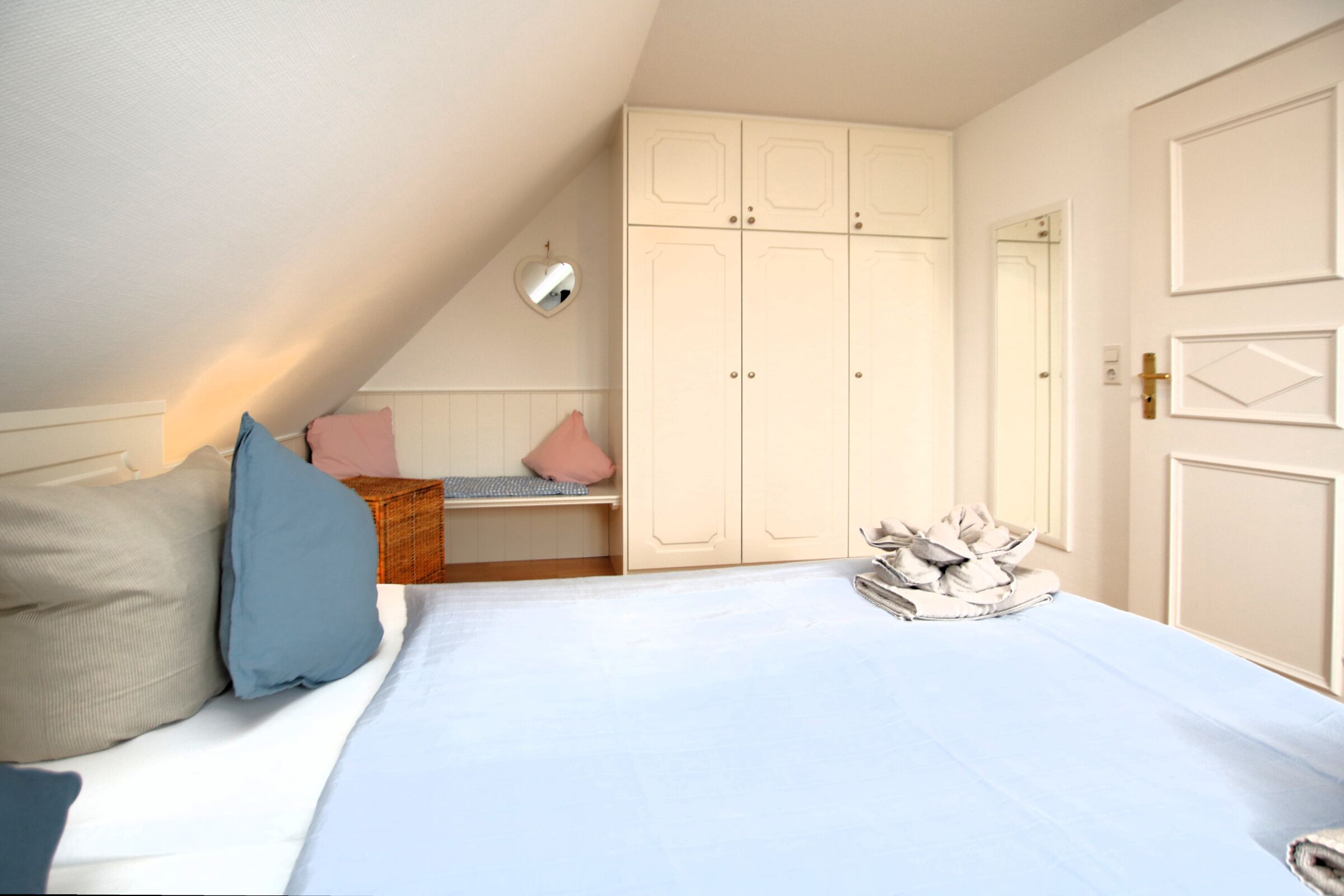 Un dormitorio con cama, almohadas, mesita de noche, armario y espejo.