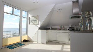 Una cocina moderna con armarios blancos, una campana extractora de acero inoxidable y vistas al océano a través de amplios ventanales.