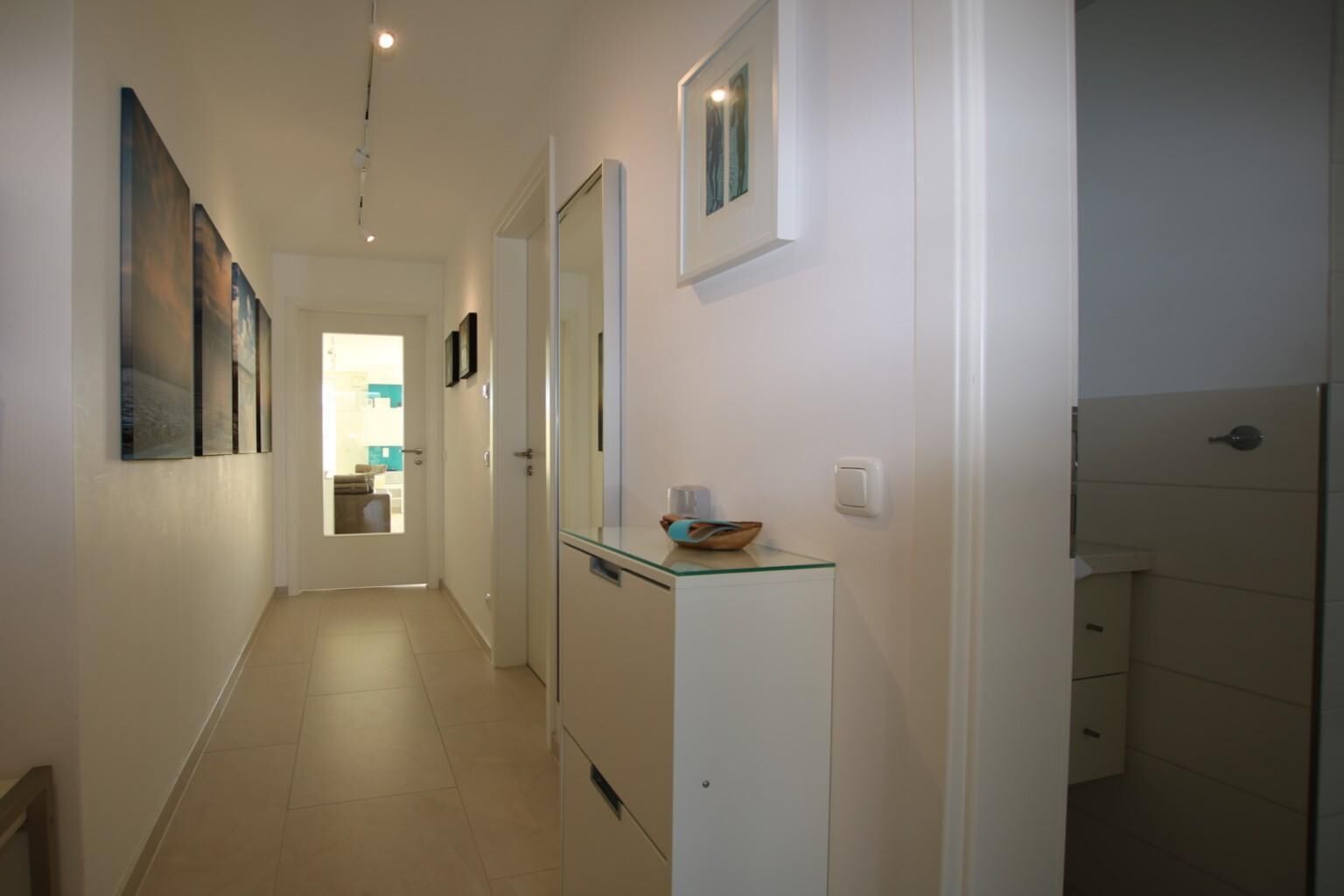 A narrow hallway with a glass-top cabinet and a door leading to a bathroom.