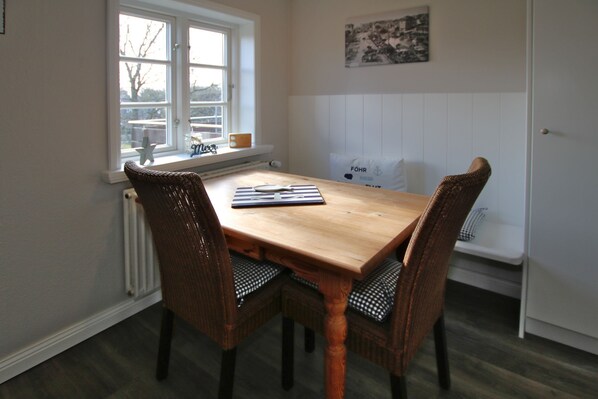 Un'area pranzo con un tavolo in legno e sedie in vimini, una finestra con vista e un muro bianco con un quadro incorniciato.